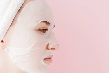Güzel genç kadın kozmetik doku maske pembe bir arka plan üzerinde bir yüzünde uyguluyor. Sağlık ve güzellik tedavi ve teknoloji kavramı