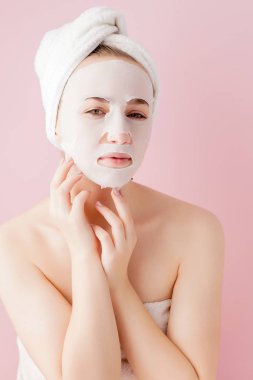 Güzel genç kadın kozmetik doku maske pembe bir arka plan üzerinde bir yüzünde uyguluyor. Sağlık ve güzellik tedavi ve teknoloji kavramı