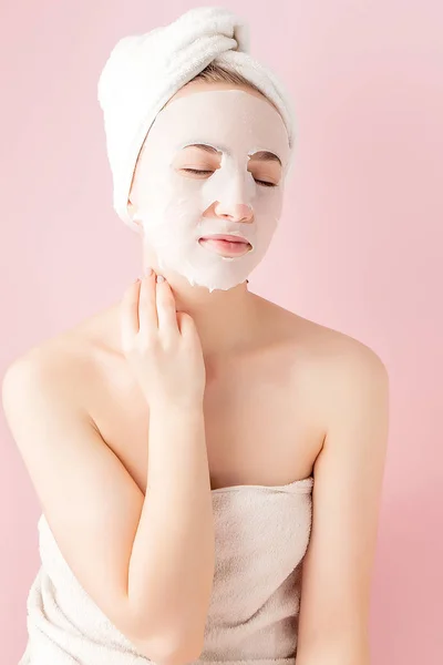 Hermosa mujer joven está aplicando una máscara de tejido cosmético en una cara sobre un fondo rosa. Salud y belleza tratamiento y concepto de tecnología —  Fotos de Stock