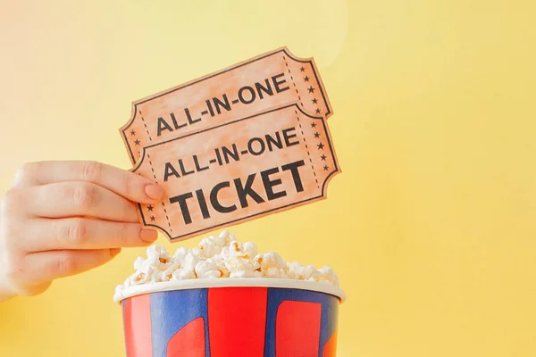 Hand tar en biobiljett och popcorn från en papperskopp på en gul bakgrund. Kvinnan äter popcorn. Filmkoncept. Ett platt ligg. Kopiera utrymme — Stockfoto