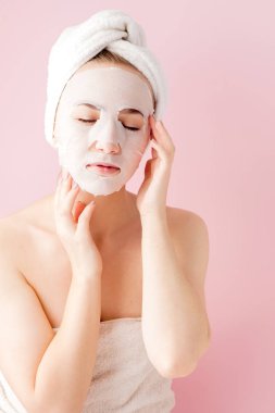 Güzel genç kadın kozmetik doku maske pembe bir arka plan üzerinde bir yüzünde uyguluyor. Sağlık ve güzellik tedavi ve teknoloji kavramı