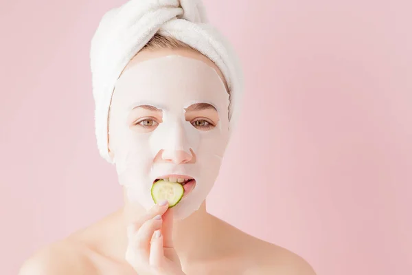 Hermosa mujer joven está aplicando una máscara de tejido cosmético en una cara sobre un fondo rosa. Salud y belleza tratamiento y concepto de tecnología — Foto de Stock