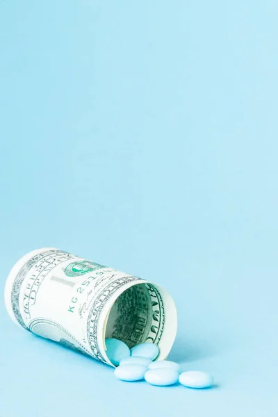 Money dollar rolled up with pills flowing out isolated on blue background, high costs of expensive medication concept. Copy space — Stock Photo, Image