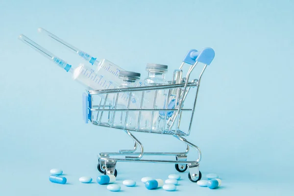 Pills and medical injection in shopping trolley on blue backgrou