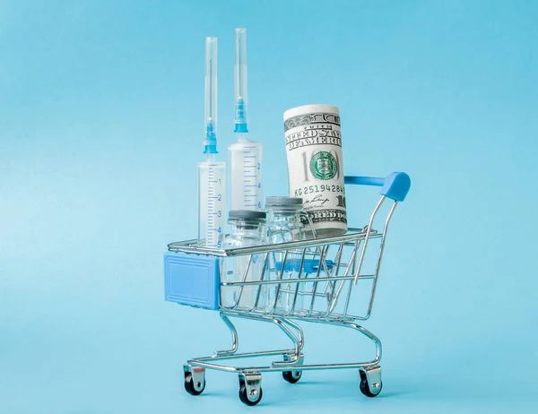 Medische injectie en dollars in winkelwagentje op blauwe backgr — Stockfoto