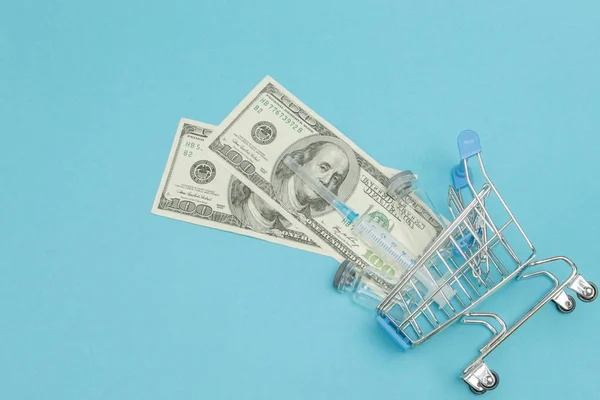 Medical injection and dollars in shopping trolley on blue backgr