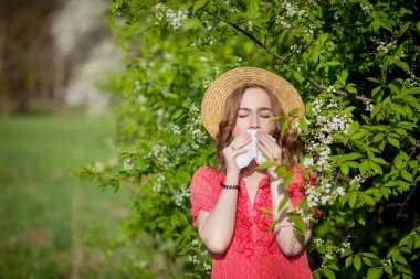Genç kız sümkürme ve çiçek açan ağacın önünde mendile hapşırma. İnsanları etkileyen mevsimsel alerjik maddeler. Güzel bayanın rhinitis 'i var..