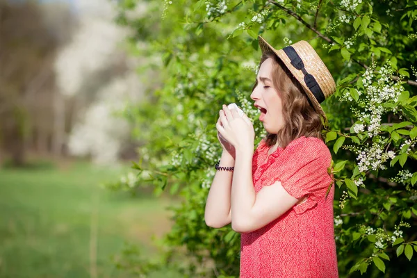 Jong meisje snuit neus en niest in weefsel voor de bloeiende boom. Seizoensgebonden allergenen die mensen beïnvloeden. Mooie dame heeft rhinitis. — Stockfoto