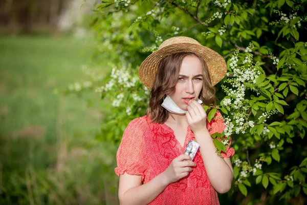 Ung flicka blåser näsa och nyser i vävnad framför blommande träd. Säsongsbundna allergener som påverkar människor. Vacker dam har rinit. — Stockfoto