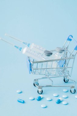 Hap ve alışveriş arabası mavi arka plan üzerinde tıbbi enjeksiyon. Sağlık bakım maliyeti, eczane, sağlık sigortası ve ilaç firması iş kavramı için yaratıcı bir fikir. Kopya alanı