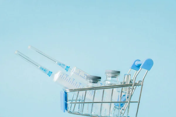 Medical injection in shopping trolley on blue background. Creative idea for health care cost, drugstore, health insurance and pharmaceutical company business concept. Copy space