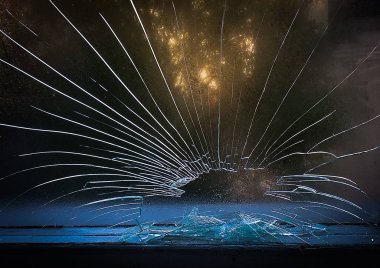 Savaş çekimi sırasında pencere camında bir mermi atışı ile delik. Delik etrafında yayılan çatlaklar. Cam tarafından bulanık ağaçlar yeşil yaprakları. Kirli pencere çerçevesi. İçeriden bir sokağın görünümü