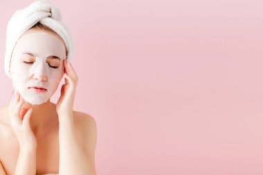 Güzel genç kadın kozmetik doku maske pembe bir arka plan üzerinde bir yüzünde uyguluyor. Sağlık ve güzellik tedavi ve teknoloji kavramı