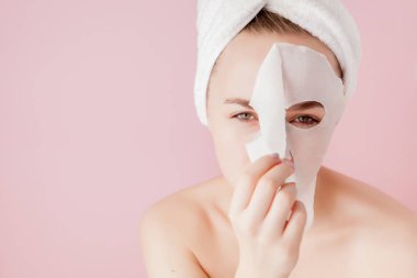 Güzel genç kadın kozmetik doku maske pembe bir arka plan üzerinde bir yüzünde uyguluyor. Sağlık ve güzellik tedavi ve teknoloji kavramı