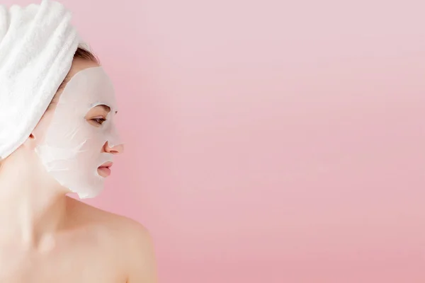 美丽的年轻女子正在涂上一个化妆品组织面膜的脸上的粉红色的背景。医疗和美容护理及技术理念 — 图库照片
