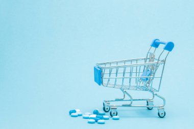 Hap ve mavi arka plan üzerinde alışveriş arabası. Sağlık bakım maliyeti, eczane, sağlık sigortası ve ilaç firması iş kavramı için yaratıcı bir fikir. Kopya alanı