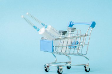 Mavi arka planda alışveriş arabası tıbbi enjeksiyon. Sağlık maliyeti, eczane, sağlık sigortası ve ilaç şirketi iş kavramı için yaratıcı fikir. Boşluk Kopyala