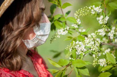 Genç kız sümkürme ve çiçek açan ağacın önünde mendile hapşırma. İnsanları etkileyen mevsimsel alerjik maddeler. Güzel bayanın rhinitis 'i var..