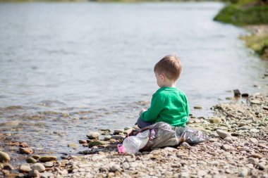 Çevre kavramını kaydedin, küçük bir çocuk çöpleri ve plastik şişeleri toplayıp çöpe atıyor..