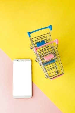 Pastel pembe boş ekran beyaz cep telefonu ve alışveriş arabaları a