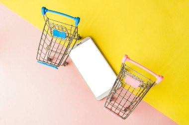 Pastel pembe boş ekran beyaz cep telefonu ve alışveriş arabaları a