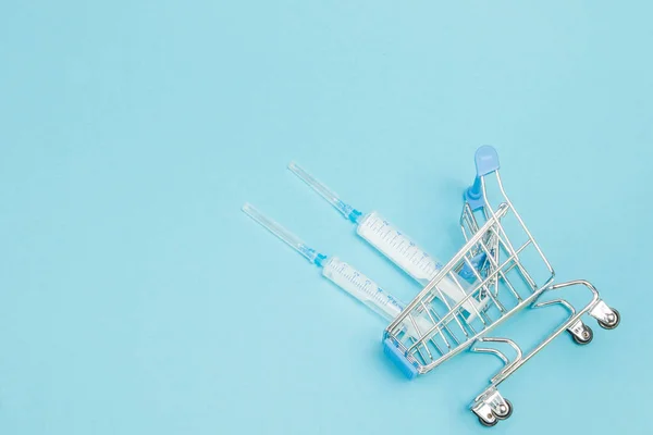 Medical injection in shopping trolley on blue background. Creati