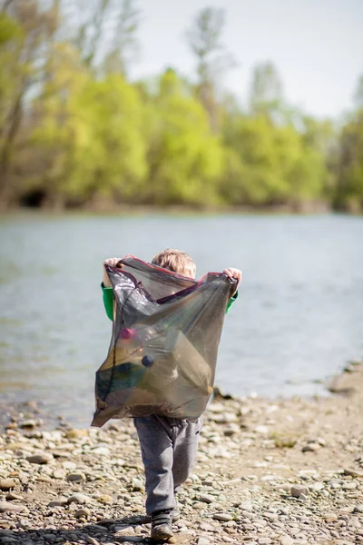 Save Environment Konzept, ein kleiner Junge sammelt Müll und Plastikflaschen am Strand, um sie in den Müll zu werfen. — Stockfoto