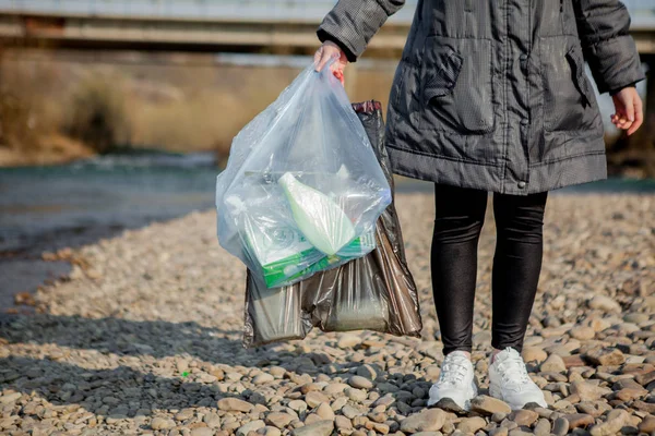 garbage in the nature, cleaning the environment in the spring on the river from the rubbish a woman in disposable latex blue mittens in to blue large plastic bag