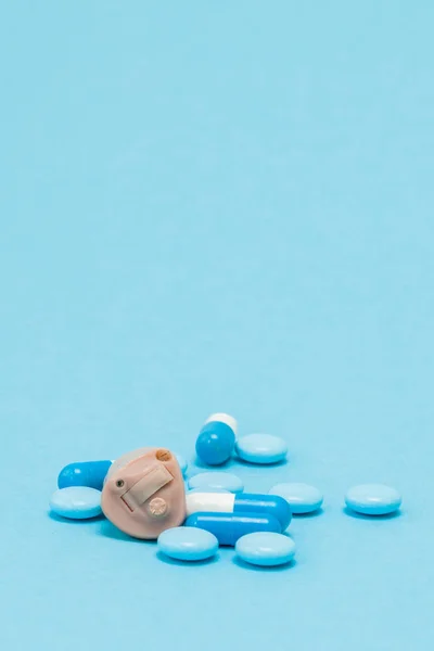 Audífono y pastillas azules sobre fondo azul. Médico, farmacia —  Fotos de Stock