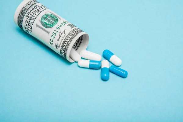Dinheiro dólar enrolado com pílulas fluindo para fora isolado em azul b — Fotografia de Stock