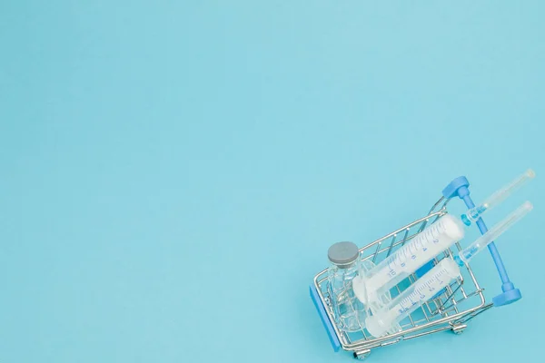 Medical injection in shopping trolley on blue background. Creati