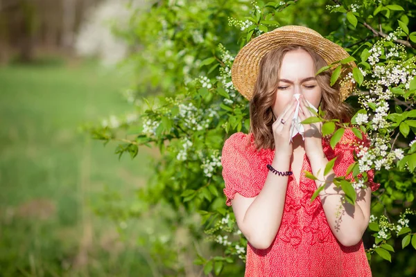 Young girl blowing nose and sneezing in tissue in front of bloom — Stock Photo, Image