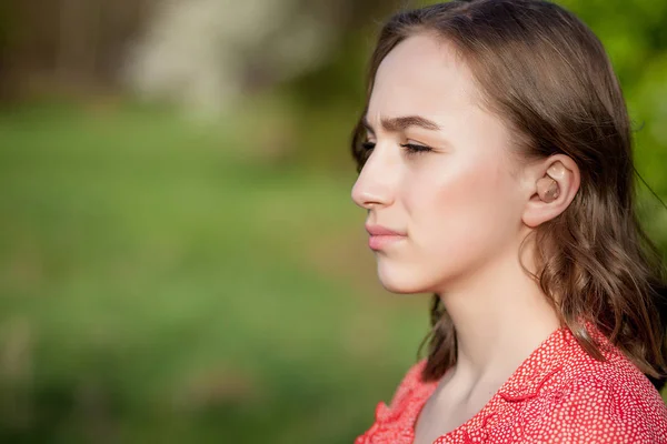 Close-up Of Female Hands Putting Hearing Aid In Ear. Modern digital in the ear hearing aid for deafness and the hard of hearing patients