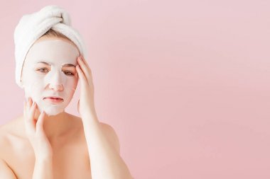 Güzel genç kadın kozmetik doku maske pembe bir arka plan üzerinde bir yüzünde uyguluyor. Sağlık ve güzellik tedavi ve teknoloji kavramı
