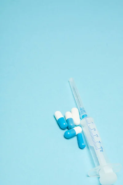 Cápsulas médicas y jeringa sobre fondo azul, con espacio para copiar — Foto de Stock