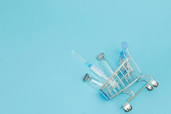 Medical injection in shopping trolley on blue background. Creati