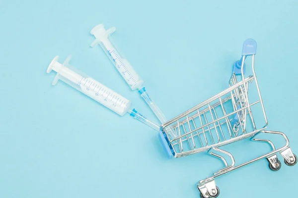 Medical injection in shopping trolley on blue background. Creati