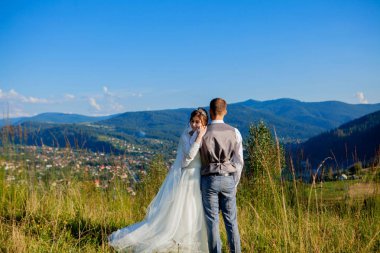 Yeni evliler gülümseme ve diğer her dağın zirvesinde çayır arasında sarıl. Düğün yürüyüş dağlar, nazik duygular çift, Sevgililer günü için fotoğraf ormanda