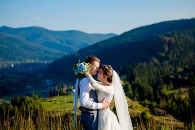 Yeni evliler gülümseme ve diğer her dağın zirvesinde çayır arasında sarıl. Düğün yürüyüş dağlar, nazik duygular çift, Sevgililer günü için fotoğraf ormanda