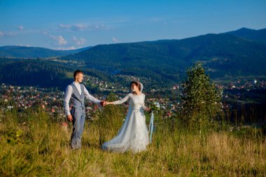 Yeni evliler gülümseme ve diğer her dağın zirvesinde çayır arasında sarıl. Düğün yürüyüş dağlar, nazik duygular çift, Sevgililer günü için fotoğraf ormanda