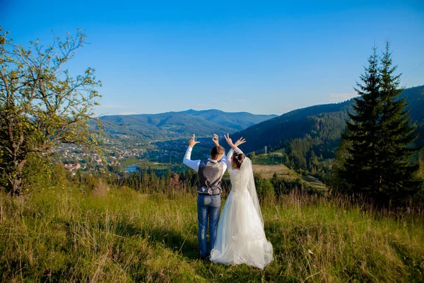 Gli sposi sorridono e si abbracciano tra i prati in cima alla montagna. Passeggiata nuziale nei boschi in montagna, le dolci emozioni della coppia, foto per San Valentino — Foto Stock