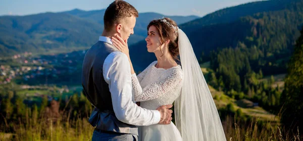 Newlyweds smile and hug each other among the meadow on top of the mountain. Wedding walk in the woods in the mountains, the gentle emotions of the couple, photo for Valentine\'s Day