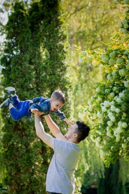 Genç babası ve gülümseyen oğlu parkta, sarılıyor ve eğleniyorlar.