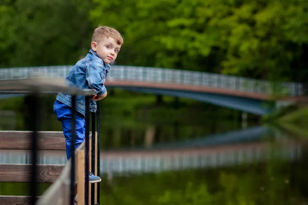 Ein kleiner Junge klettert auf ein Brückengeländer im Park. die Bedrohung durch — Stockfoto