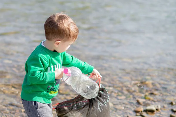Αποθήκευση έννοια του περιβάλλοντος, ένα μικρό αγόρι συλλογή σκουπίδια και πλαστικά μπουκάλια στην παραλία για να πετάξει στα σκουπίδια. — Φωτογραφία Αρχείου