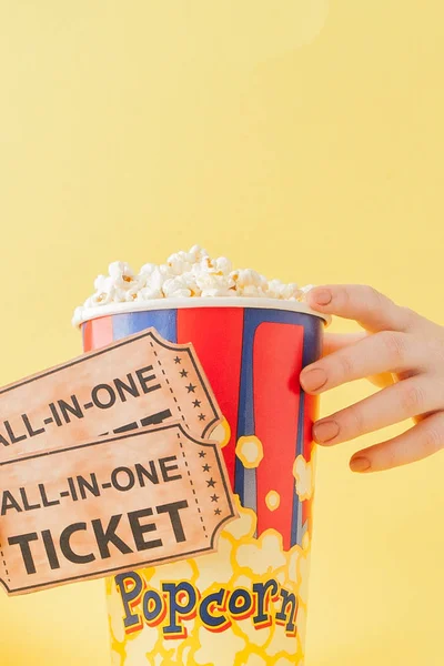 Hand tar en biobiljett och popcorn från en papperskopp på en gul bakgrund. Kvinnan äter popcorn. Filmkoncept. Ett platt ligg. Kopiera utrymme — Stockfoto