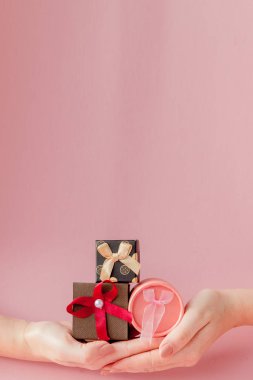 Kadınların elleri pembe bir arka plan üzerinde küçük hediye kutuları. Şenlikli 