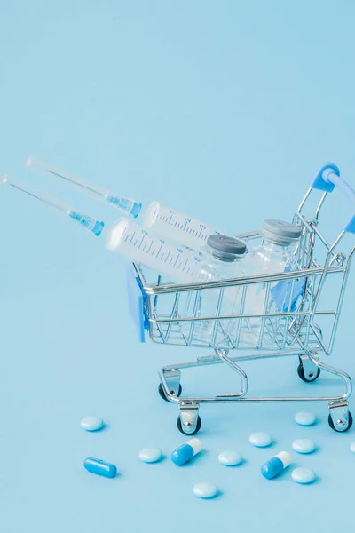 Pills and medical injection in shopping trolley on blue background. Creative idea for health care cost, drugstore, health insurance and pharmaceutical company business concept. Copy space