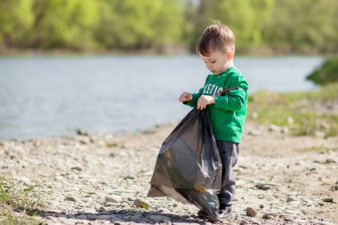 Çevre kavramını kaydedin, küçük bir çocuk çöpleri ve plastik şişeleri toplayıp çöpe atıyor..