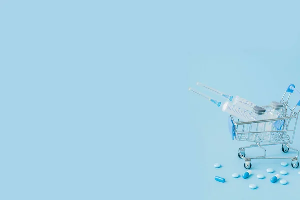 Pills and medical injection in shopping trolley on blue background. Creative idea for health care cost, drugstore, health insurance and pharmaceutical company business concept. Copy space — Stock Photo, Image